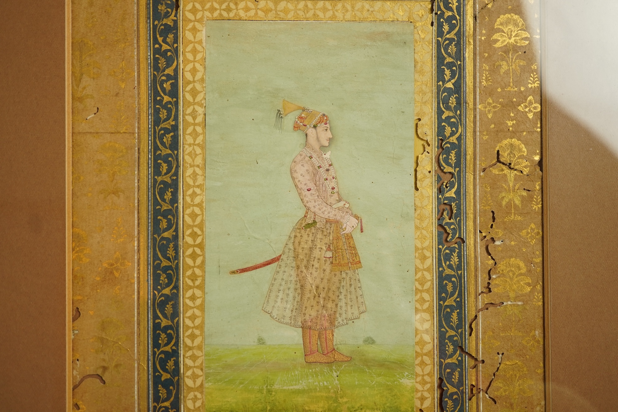 Mogul (Mughal) School , Profile Portrait of a Mogul dignitary, possibly Shah Jahan (1592-1666), full length, wearing court attire and a sword, standing in a landscape, watercolour miniature, 31cm x 20.5cm including borde